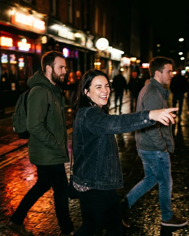 Three friends walking down a wet city street at night, one pointing ahead